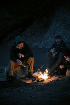 three people sitting around a campfire in the dark, with one person lighting a candle