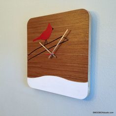 a wooden clock with a red bird sitting on it's face and two sticks sticking out of the back