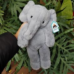 an elephant stuffed animal being held by someone's hand in front of green leaves