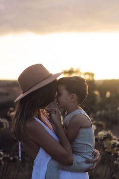 a woman holding a small child in her arms while the sun is setting behind them