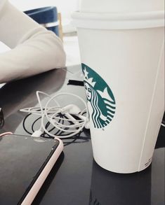 a cup of coffee sitting on top of a table next to a cell phone and headphones