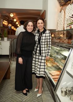 two women standing next to each other in front of a display case with donuts