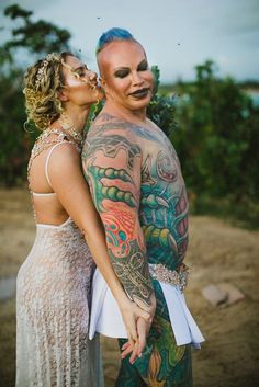 a man and woman standing next to each other with tattoos on their body, both holding hands