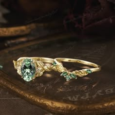 two gold rings with green and white stones sitting on top of a table next to a clock