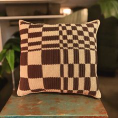 a brown and white checkered pillow sitting on top of a wooden table next to a green plant