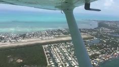 an airplane wing flying over a city and ocean