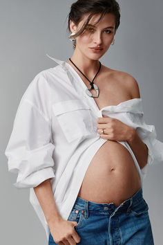 a pregnant woman wearing a white shirt and jeans is holding her belly in one hand