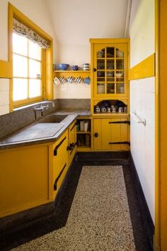 a kitchen with yellow cabinets and black flooring is shown in this image, there are dishes on the shelves