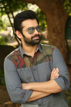 a man with his arms crossed standing in front of a tree