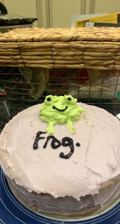 a cake with frosting and a frog on it sitting on a plate in front of a basket