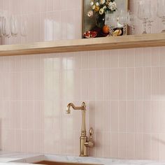 a kitchen with pink tiles and gold faucet, wine glasses on the shelf