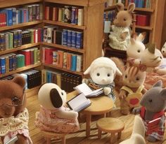 several stuffed animals are sitting at a table in front of bookshelves and chairs