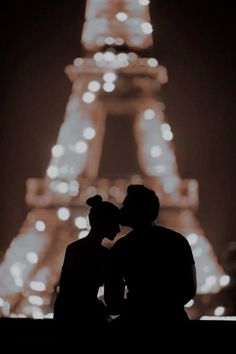 two people sitting in front of the eiffel tower at night with their backs to each other