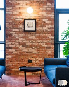 a living room with two blue couches and a coffee table in front of a brick wall