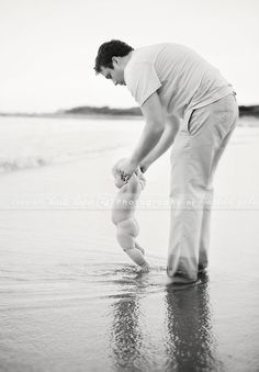 a man holding a baby while standing on top of a beach