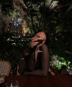 a woman sitting at a table holding a wine glass in front of her face and looking up