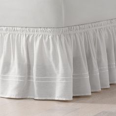 a white bed skirt with ruffles on the top and bottom, sitting on a hard wood floor