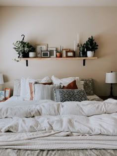 a bed with white sheets, pillows and plants on the shelves above it in a bedroom