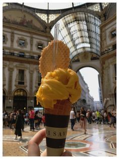 a hand holding an ice cream sundae with waffles on top in front of a building