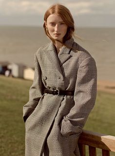 a woman standing on a wooden bench next to the ocean wearing a coat and pants