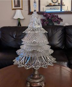 a glass christmas tree sitting on top of a wooden table next to a black couch