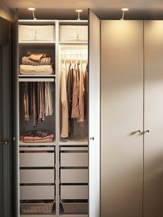 an open closet with clothes hanging on the doors and drawers, in front of a window