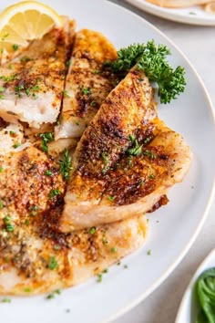 a white plate topped with chicken and garnished with parsley next to lemon wedges