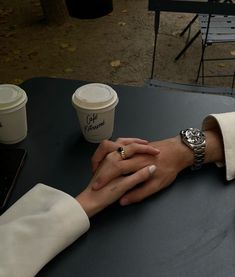 two people holding hands with coffee cups in the background