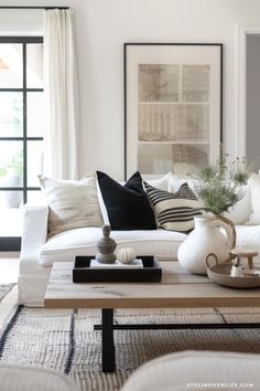 a living room filled with white furniture and black and white pillows on top of a coffee table