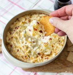 a hand holding a cracker over a bowl of dip