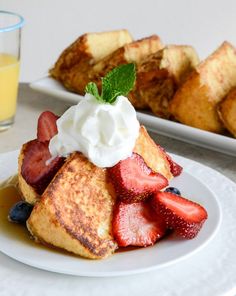 french toast with whipped cream and strawberries on a plate next to a glass of orange juice