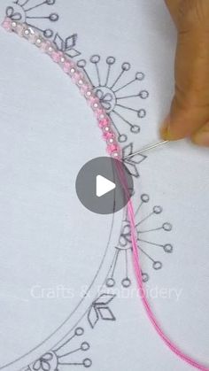 someone is stitching something with pink thread and beads on top of a white t - shirt