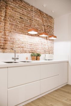 a white kitchen with brick wall and wooden flooring in the center, surrounded by hanging lights