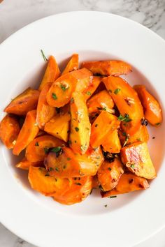 a white bowl filled with cooked carrots on top of a marble countertop next to a knife and fork