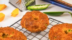 three fried food items on a cooling rack next to sliced cucumbers and green peppers