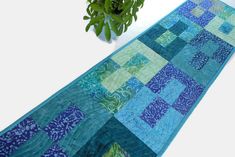 a blue and green patchwork table runner next to a potted plant