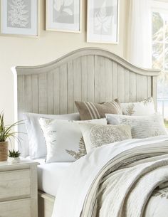 a bed with white sheets and pillows in a bedroom next to pictures on the wall