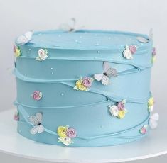 a blue frosted cake with flowers and butterflies on the icing is sitting on a white table