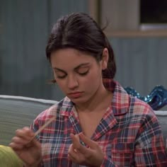 a woman sitting on a couch holding a toothbrush in her hand and looking down