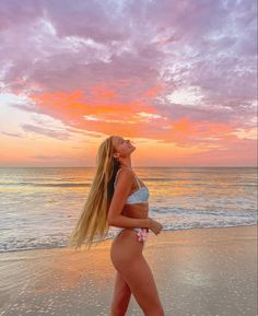 a woman standing on top of a sandy beach next to the ocean at sun set