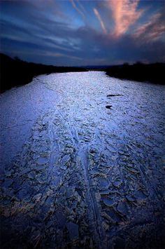 the sky is filled with clouds and blue water as it sits in the middle of an icy river