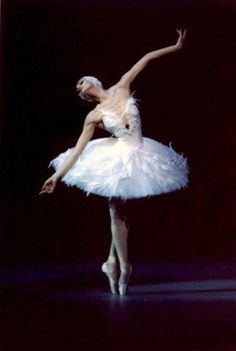 a ballerina in white tutu with her arms extended and legs spread out, standing on one leg