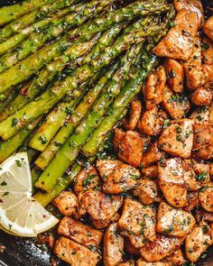 chicken and asparagus in a skillet with lemon wedges