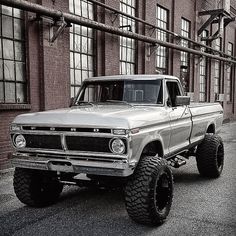 an old pick up truck parked in front of a building with large tires on it