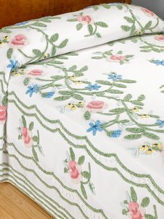 a bed covered in white and green floral bedspread with pink flowers on it