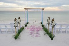 an outdoor ceremony setup on the beach with flowers and candles in front of the aisle