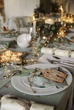 the table is set for christmas dinner with silverware and white plates, candles and napkins