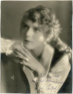 an old black and white photo of a woman with her hand on the back of a chair