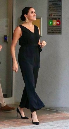 a woman in black jumpsuit walking down the street with her hand on her hip