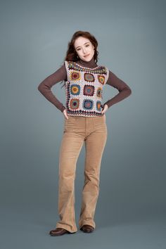 a woman standing with her hands on her hips wearing brown pants and a multicolored sweater